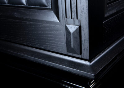 Ein schwarzer Luxus-Tresor mit handwerklicher Ledernaht auf Holz-Aufbau – Detail Fuß